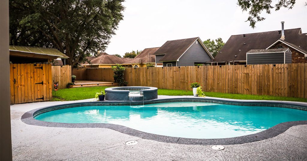 A pool with a jacuzzi in a backyard with a wood fence