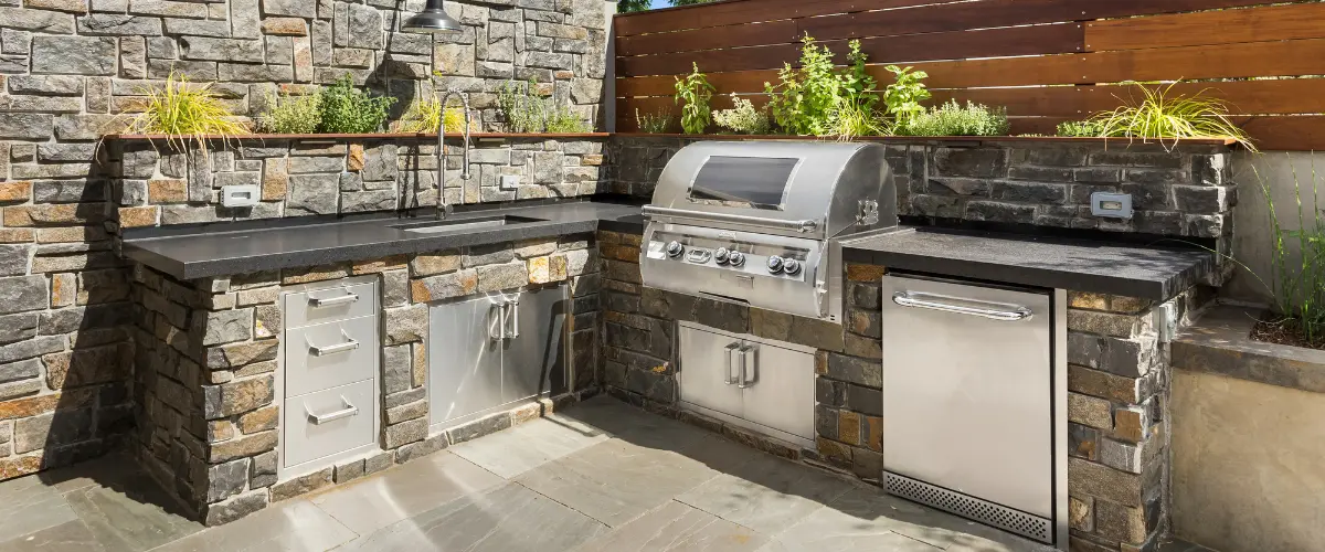 Outdoor kitchen with stone countertops, built-in grill, and storage cabinets.