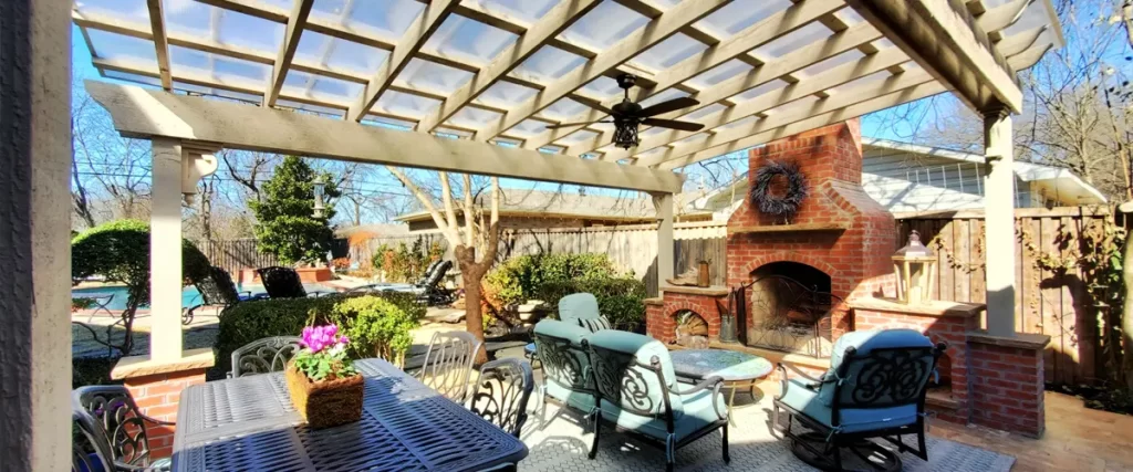 Covered backyard patio with pergola, brick fireplace, and outdoor furniture for cozy entertaining space - featured