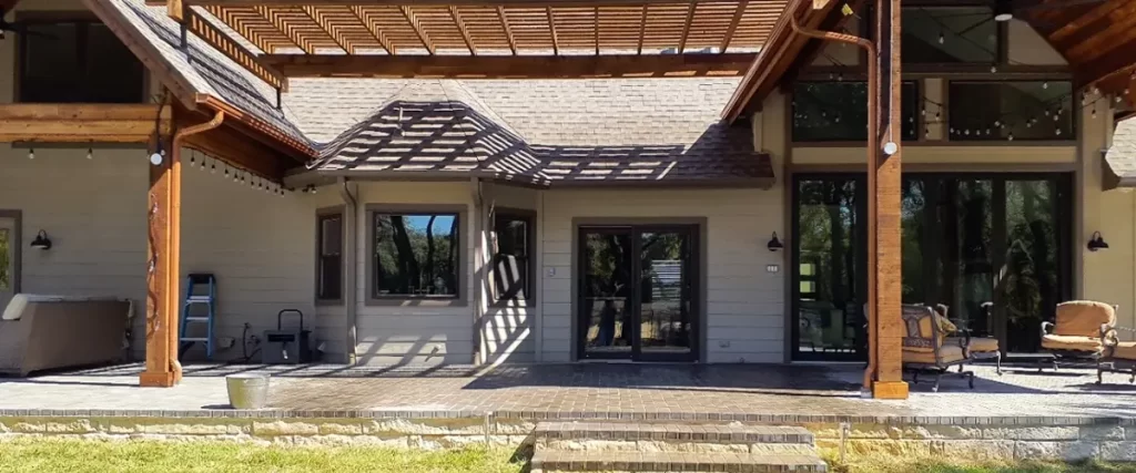 Large backyard patio with wood pergola, brick pavers, and outdoor lounge seating attached to modern farmhouse-style home