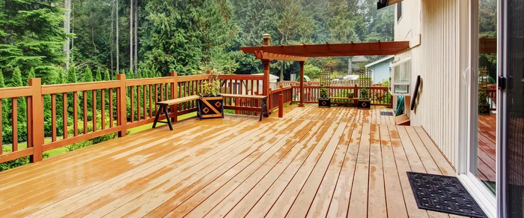 Spacious wooden backyard deck with pergola, railing, and built-in benches surrounded by evergreen trees
