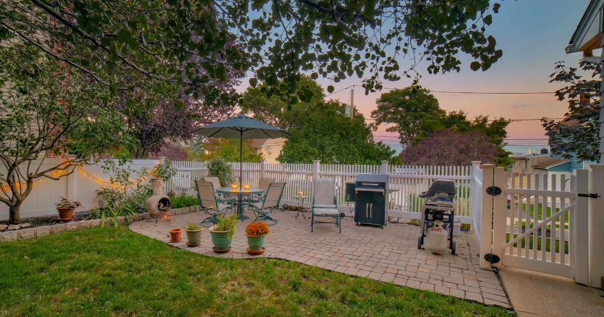 Backyard patio with seating, potted plants, and a grill at sunset