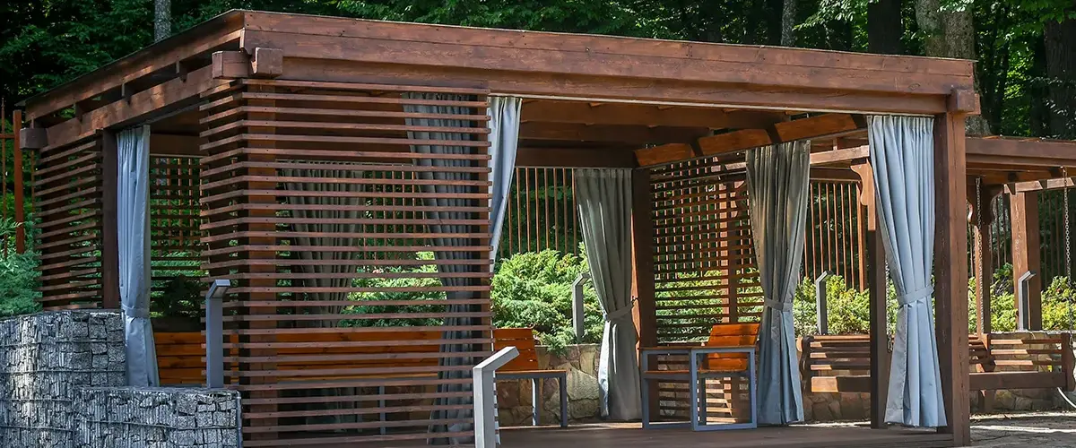 Wooden cabana-style pergola with slatted walls and curtains