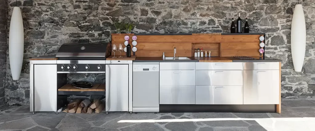 Outdoor kitchen with stainless steel grill, dishwasher, and modern cabinets against stone wall