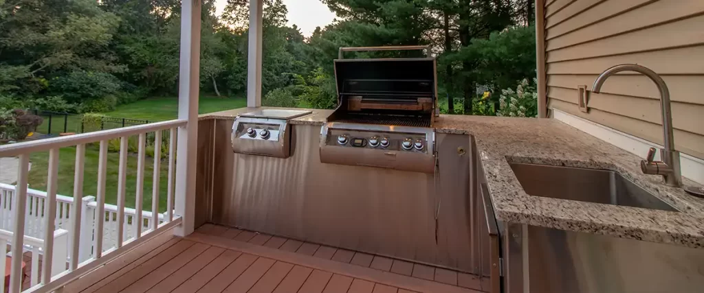 Outdoor kitchen with stainless steel grill and granite countertop with sink