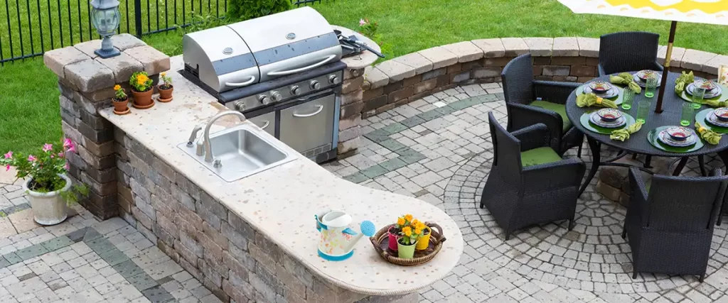 Stone outdoor kitchen with sink, grill, and dining area on paver patio