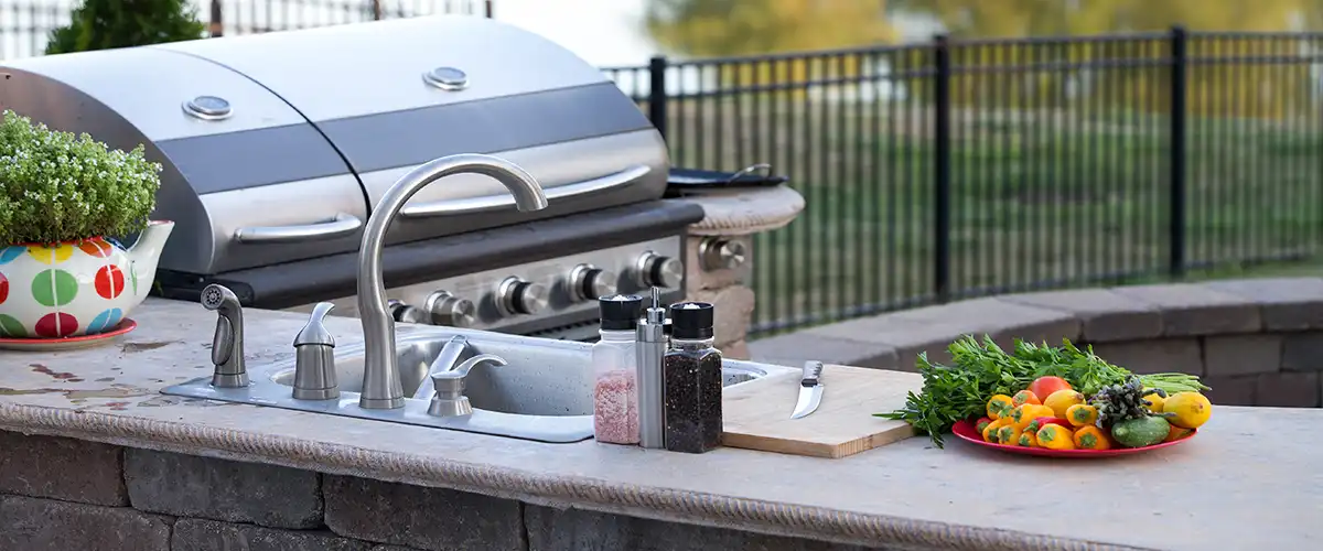 Outdoor kitchen countertop with sink, grill, and fresh vegetables setup