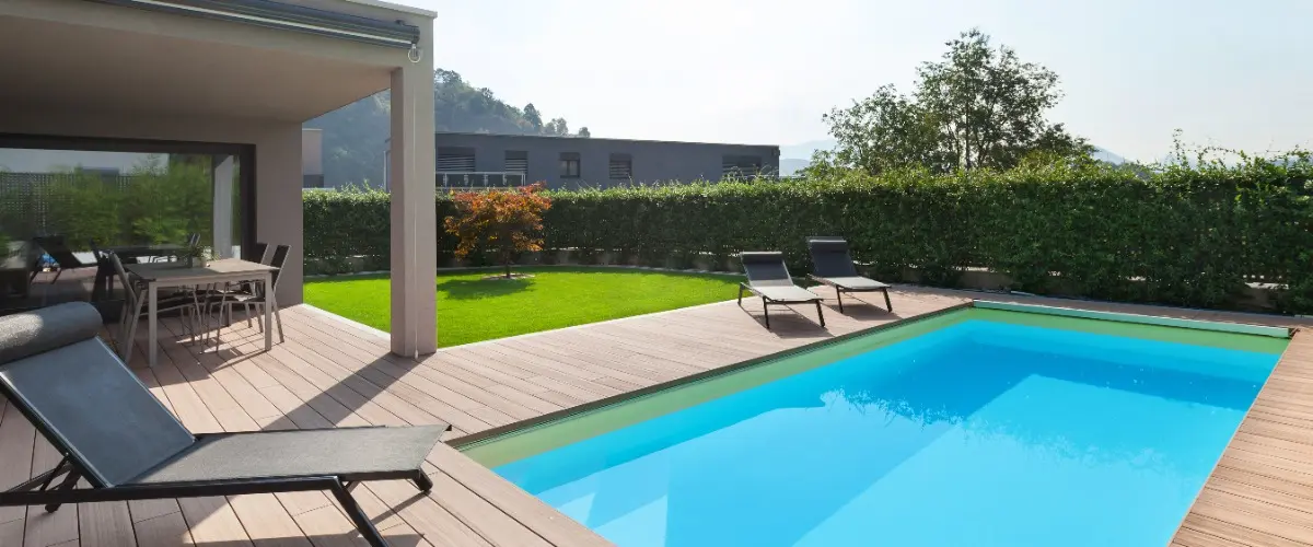 A backyard pool surrounded by a wooden deck and patio furniture, perfect for relaxation and outdoor gatherings
