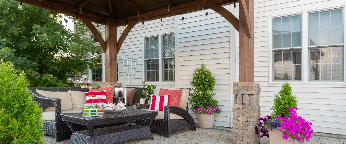 A covered patio featuring wicker furniture surrounded by colorful flowers.