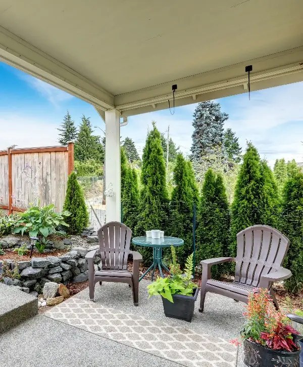 A covered patio with several chairs surrounded by a lush garden.