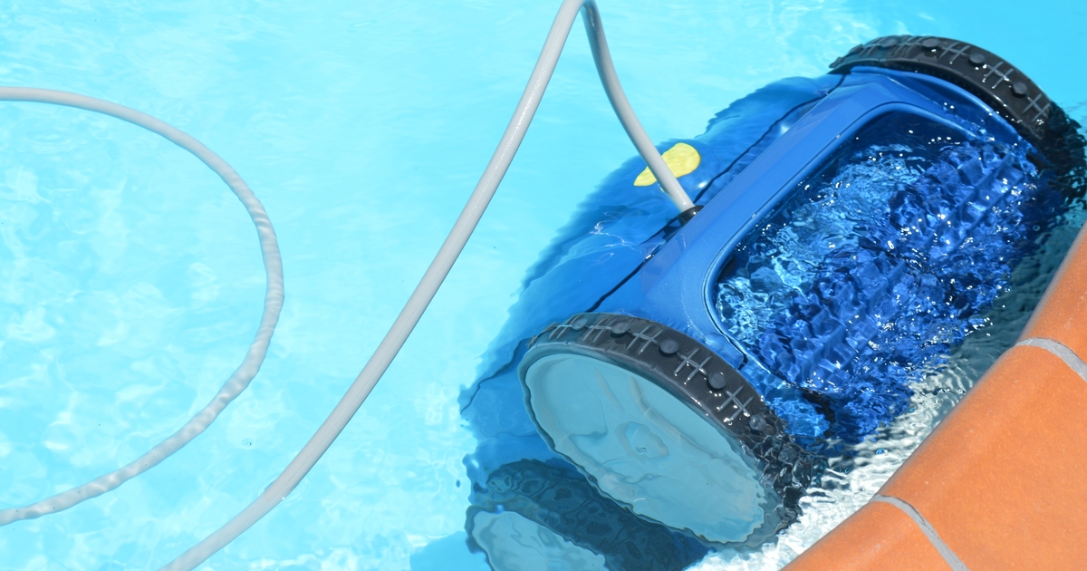 A blue robotic pool cleaner submerged in a bright blue swimming pool, working to keep the water clean. This represents one component of energy-efficient pool systems.