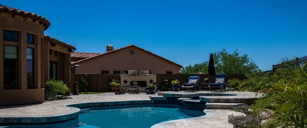 A serene pool and patio area in a home, featuring lounge chairs and greenery for relaxation and outdoor enjoyment.