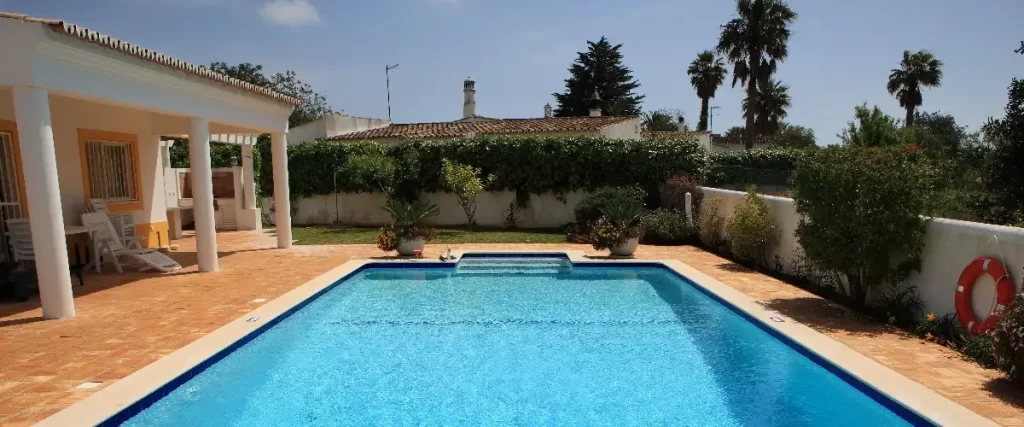 A small pool surrounded by a patio in a backyard, featuring lounge chairs and greenery.