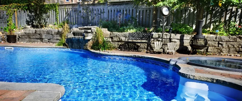 an in-ground swimming pool in a backyard featuring a blue tiled interior and is surrounded by landscaping