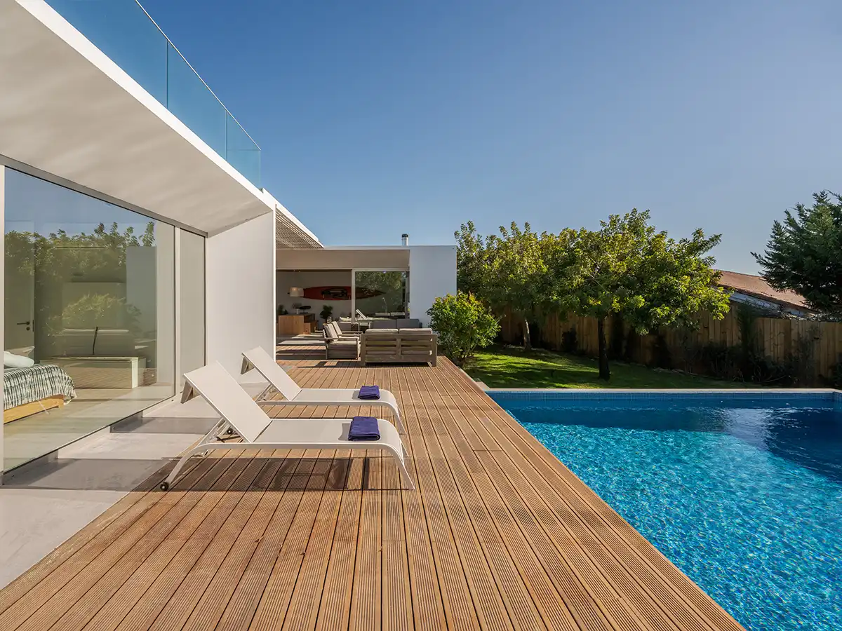 Modern poolside deck installation beside a contemporary home, showcasing wide wood decking boards and a clean, open outdoor relaxation area.