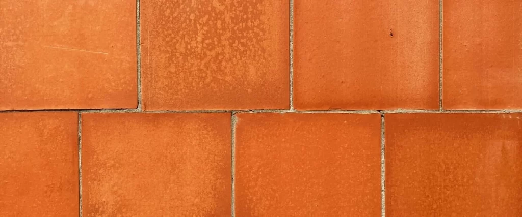 A close-up top view of authentic orange saltillo tile flooring featuring a rustic handmade texture with natural tonal variations and thin grout lines.