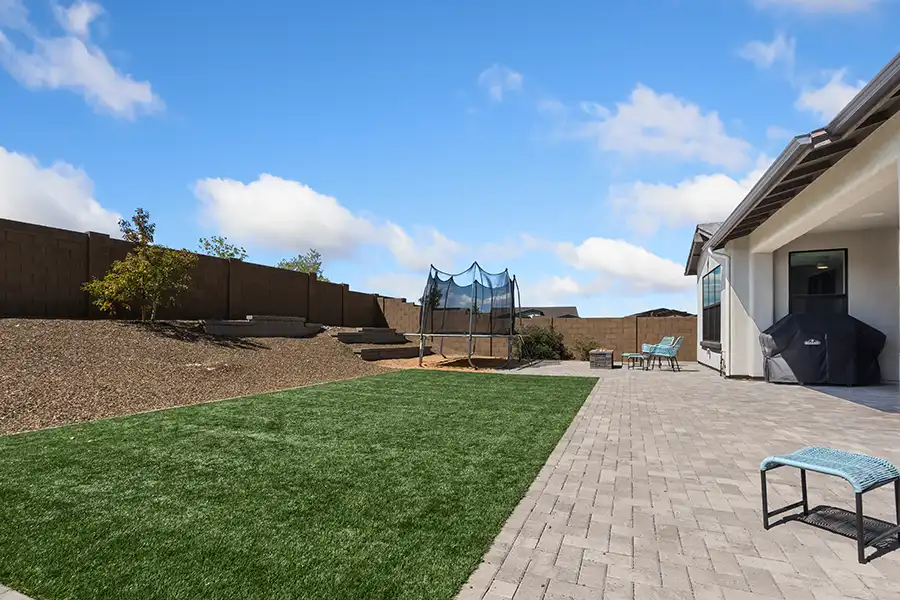Artificial turf lawn beside paver patio with trampoline and open backyard layout