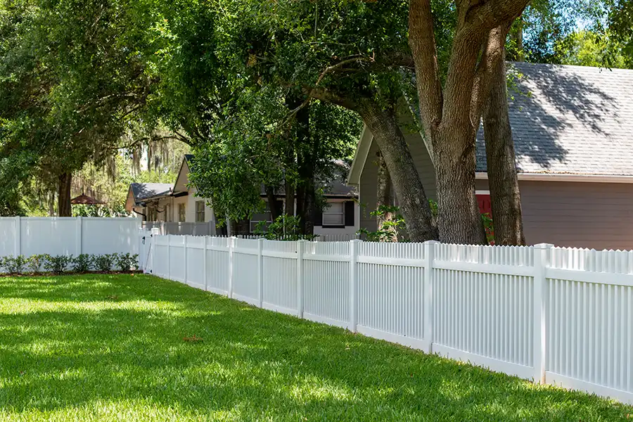 Natural grass backyard lawn with white fence and mature trees in a shaded setting