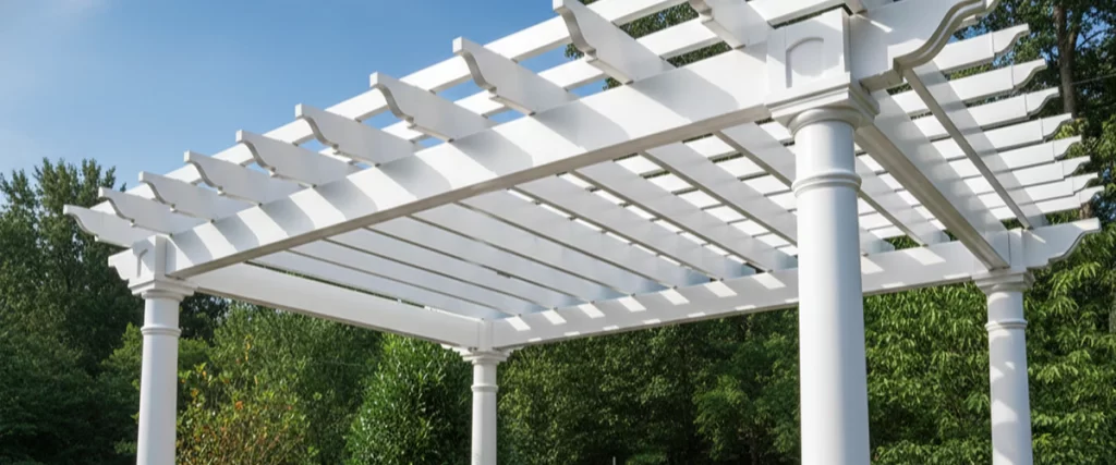 Large classic white vinyl pergola with elegant round columns set against a backdrop of lush green trees.