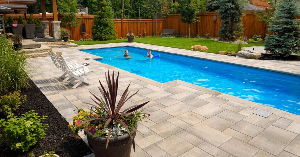A large backyard featuring a luxury inground swimming pool with various types of pool finishes and a stone paver patio.