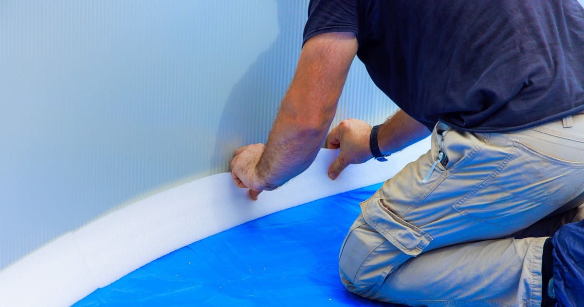 A professional pool technician carefully smoothing and fitting a new blue vinyl liner to ensure a long-lasting and durable pool surface.