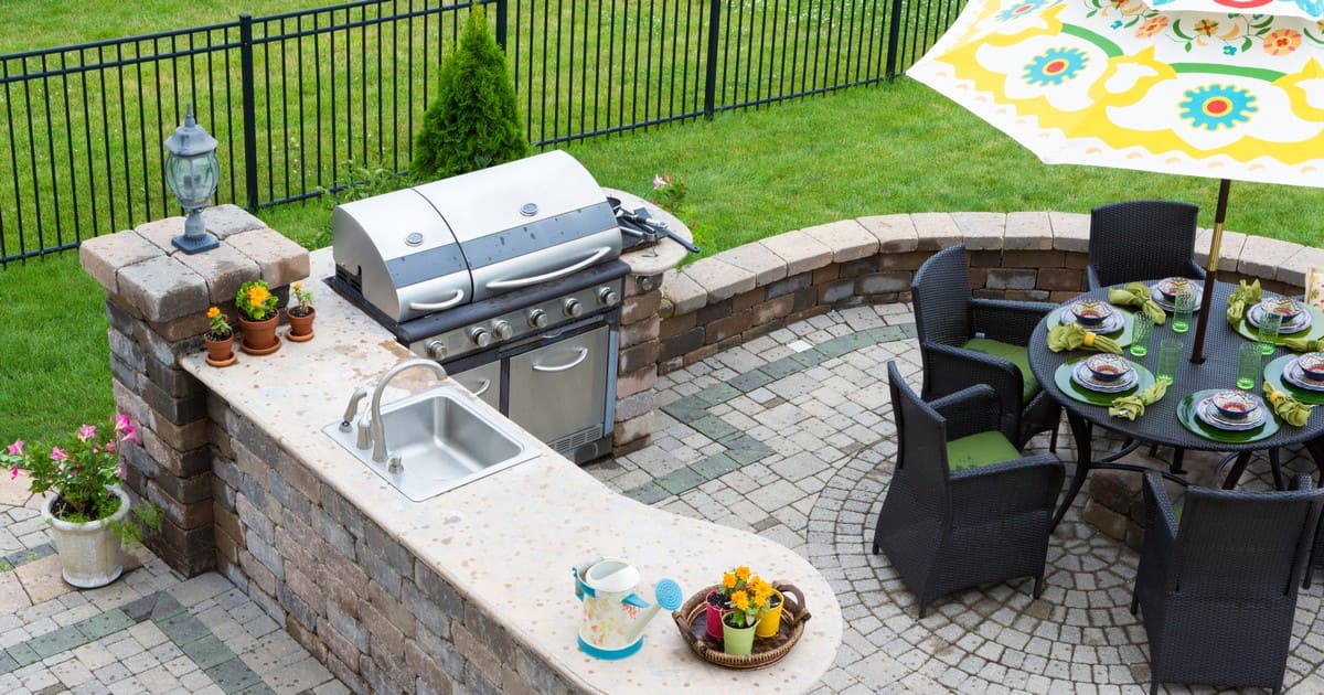 A luxurious outdoor kitchen and dining area with a large grill, stone countertops, and a shaded table to keep the patio cool in summer.