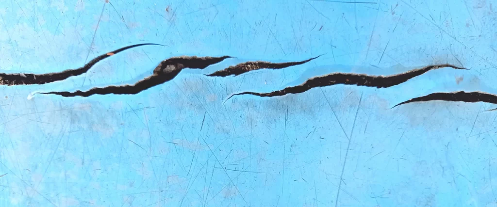 A detailed close-up shot showing deep cracks and structural wear in a blue swimming pool surface that needs repair or a new liner.