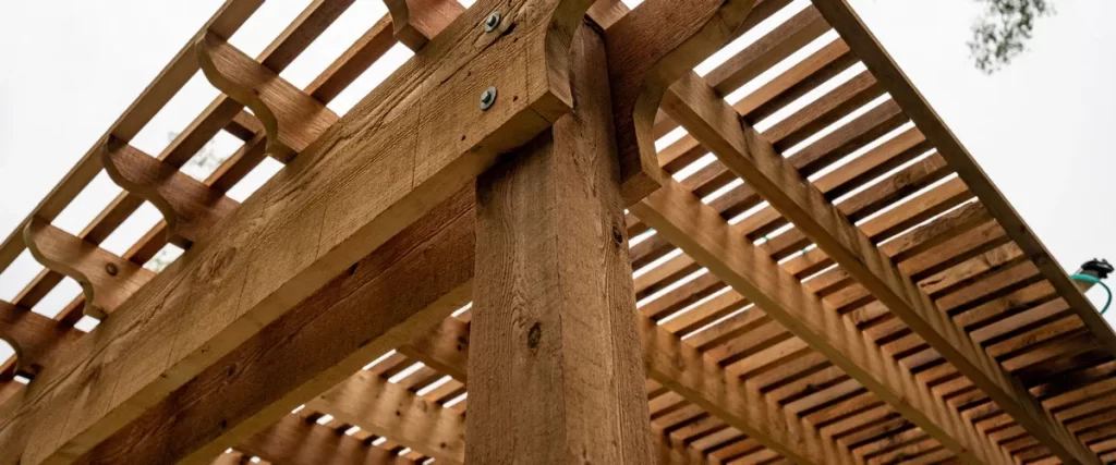Close-up view of a sturdy wood pergola built with heavy cedar beams and metal hardware against a bright sky.