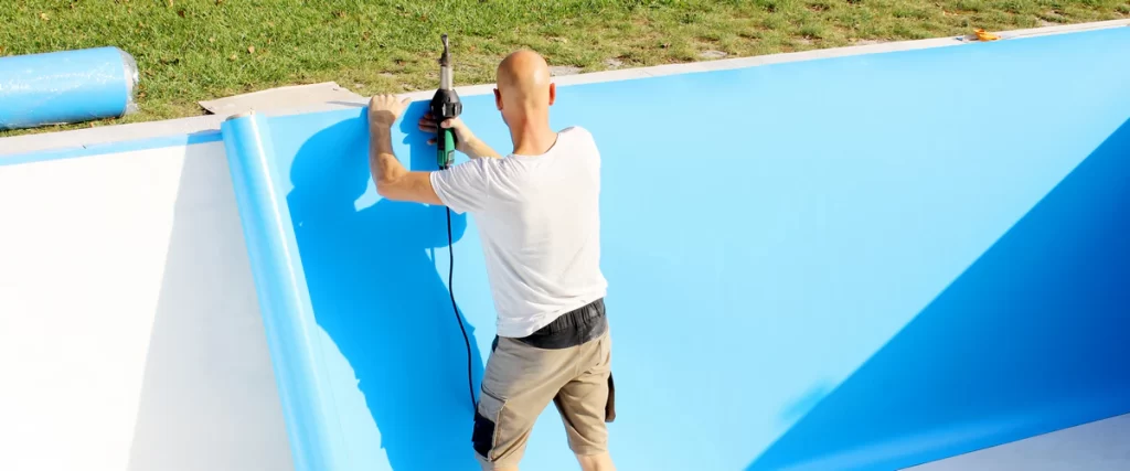 An expert pool contractor using a heat welding tool to secure blue pool liners along the interior wall of a swimming pool during a renovation.