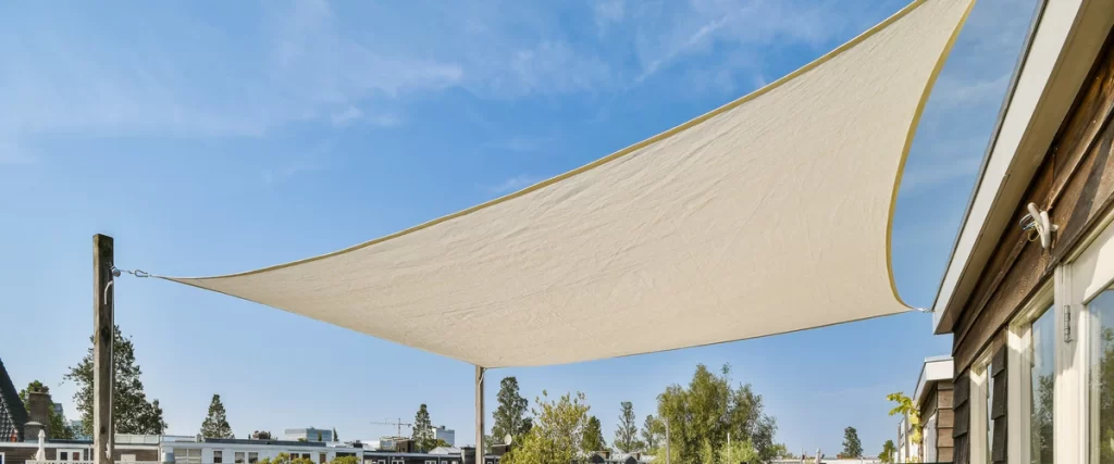 A large cream-colored triangle shade sail stretched across a backyard patio to block direct sunlight and heat.