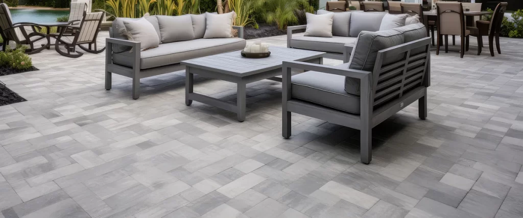 Large scale silver travertine pavers installed on a modern outdoor patio with grey wicker furniture.