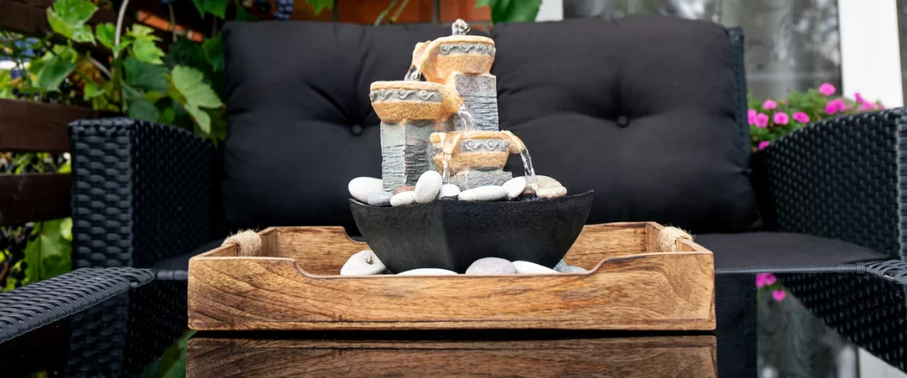 Small tiered tabletop water feature with flowing water and white river stones in a wooden tray.