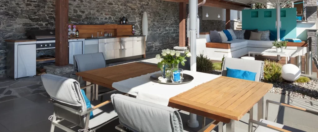 An outdoor kitchen under a covered patio featuring a large bar with stools and professional cooking equipment.