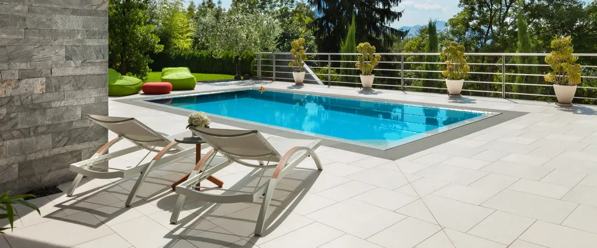 A close-up view of a crystal clear inground swimming pool with textured stone paving around the edges.