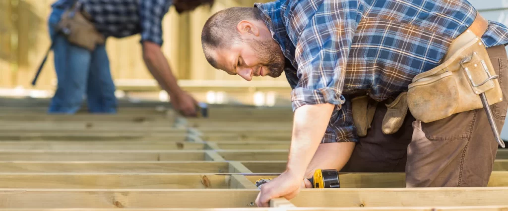 Two professional contractors installing pressure-treated wooden floor joists for a custom outdoor deck construction project.