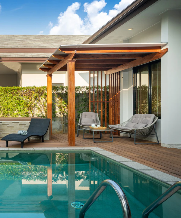 A beautifully designed backyard swimming pool featuring a wooden deck, a custom wooden pergola with a transparent roof, and modern outdoor lounge seating, created by a pool designer in McKinney, TX.