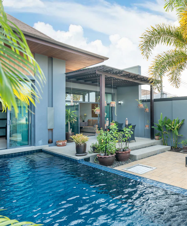 Modern dark blue rectangular swimming pool next to a grey house with a covered patio, pergola, and potted plants, created by a professional pool designer in Lewisville, TX.
