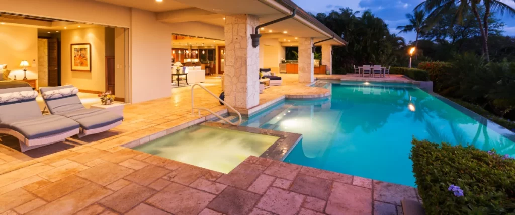A luxurious rectangular swimming pool illuminated at dusk, featuring an integrated square spa and a shallow tanning ledge right next to a high-end covered outdoor patio.
