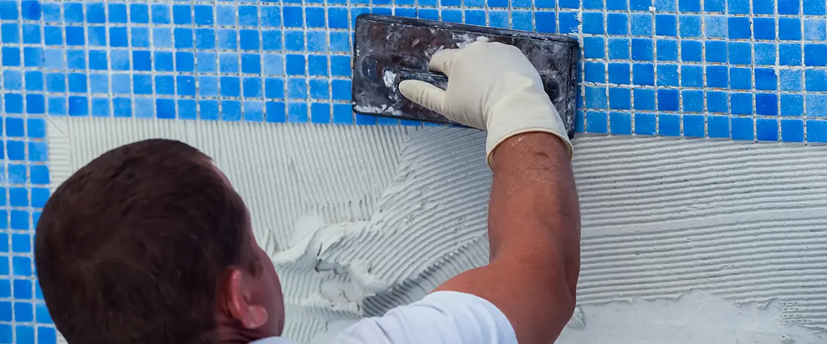 Pool tile installation with blue mosaic tiles during a custom swimming pool renovation project
