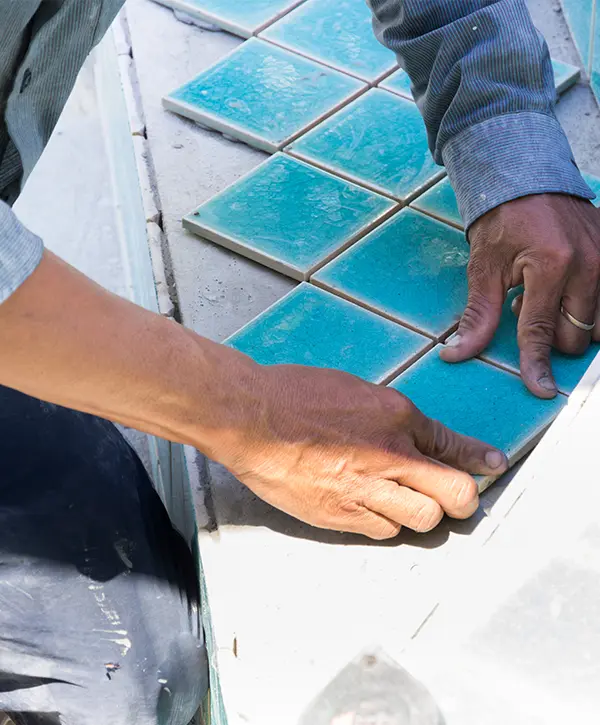 Pool tile installer placing ceramic waterline tiles during a professional swimming pool remodel